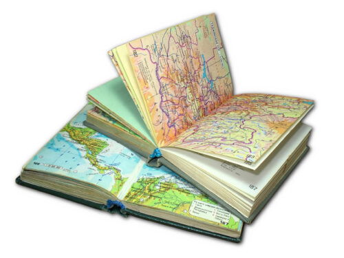 Two road atlas books open atop one another. One is a beige map with mostly red lines, while under it is a green and blue map showing northern South America and Central America