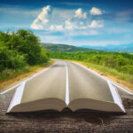 A composite image of an asphalt road forming the pages of a book, then leading to a road curving between some green hills and trees into the distance on the left. The sky behind is blue and green with big fluffy white clouds