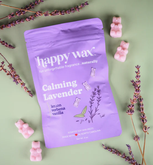 A purple bag of happy wax melts in calming lavender in a purple zip top bag against a green background with lavender sprigs. Around the bag are purple gummy bear shaped wax melts.