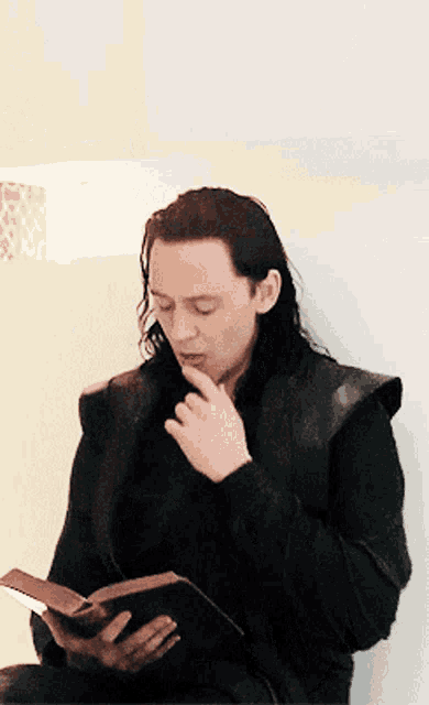 Gif of Loki, played by Tom Hiddleston, licking his finger and turning the pages of a book.