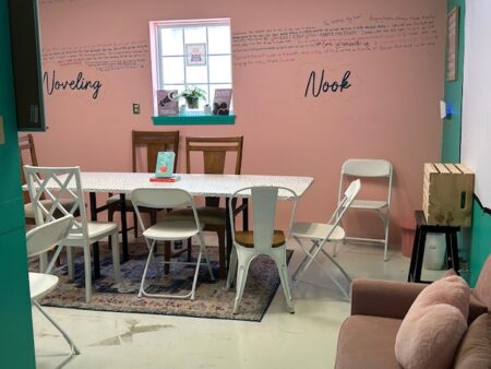 A pink room with tables and chairs and noveling nook written on the wall.