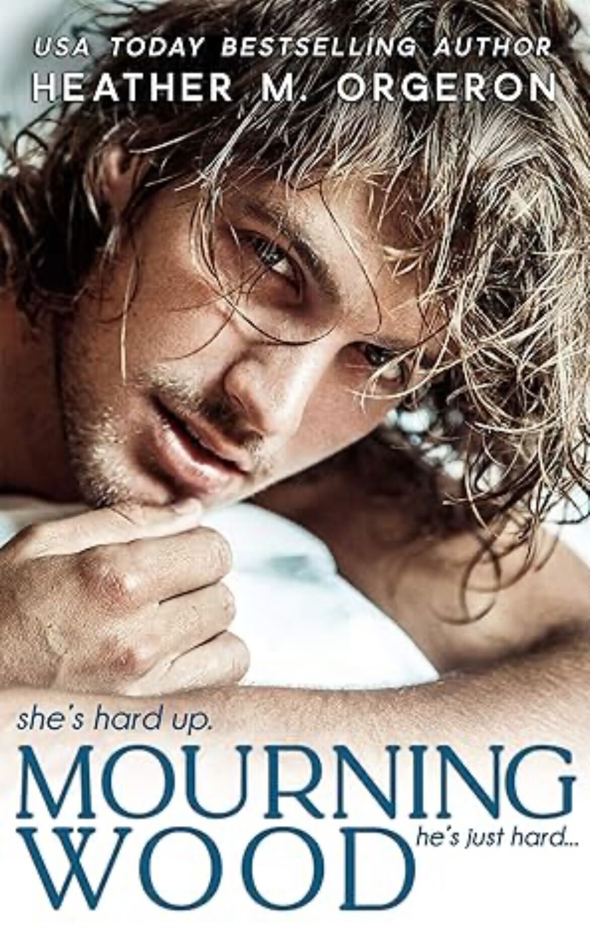 Mourning Wood by Heather M. Orgeron. A floppy haired man is looking at you from bed, peeking over a pillow. 