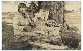 sepia-toned photo shows Ta-bu-ce demonstrating basket weaving surrounded by baskets she made