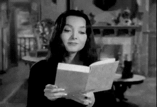 Morticia Addams reads a book and then her eyes go VERY Wide and she looks shocked