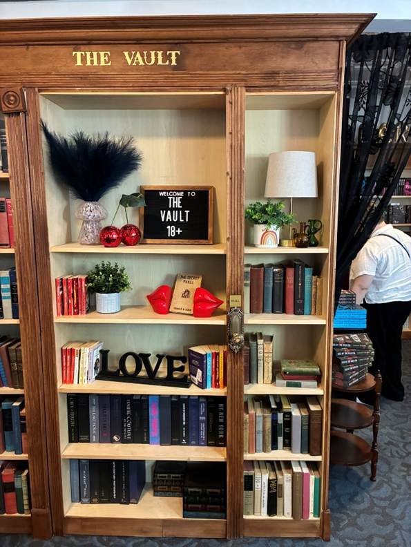 Alt: A bookshelf with a sign that says The Vault that is full of books and knickknacks.