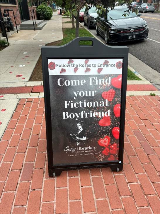 Alt text: a sandwich sign on the sidewalk that says Come Find your Fictional Boyfriend.