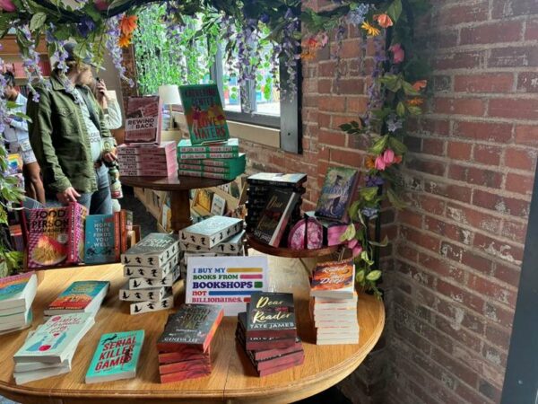 Alt: A display of books with a flower archway with a rainbow sign that says I buy my books form bookshops not billionaires.