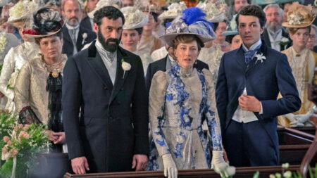George, Berth and Larry Russell in a row of pews. George has a thick beard, Bertha is wearing blue and silver with a blue and silver plumed hat, and Larry is in a top buttoned suit