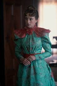 Gladys wears an aqua dress with neon pink shoulder ruffles