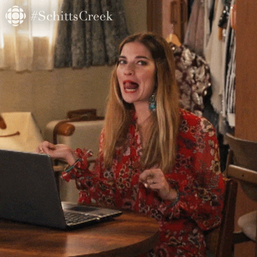 Alexis from Schitt's Creek gleefully waves her hands in front of her laptop