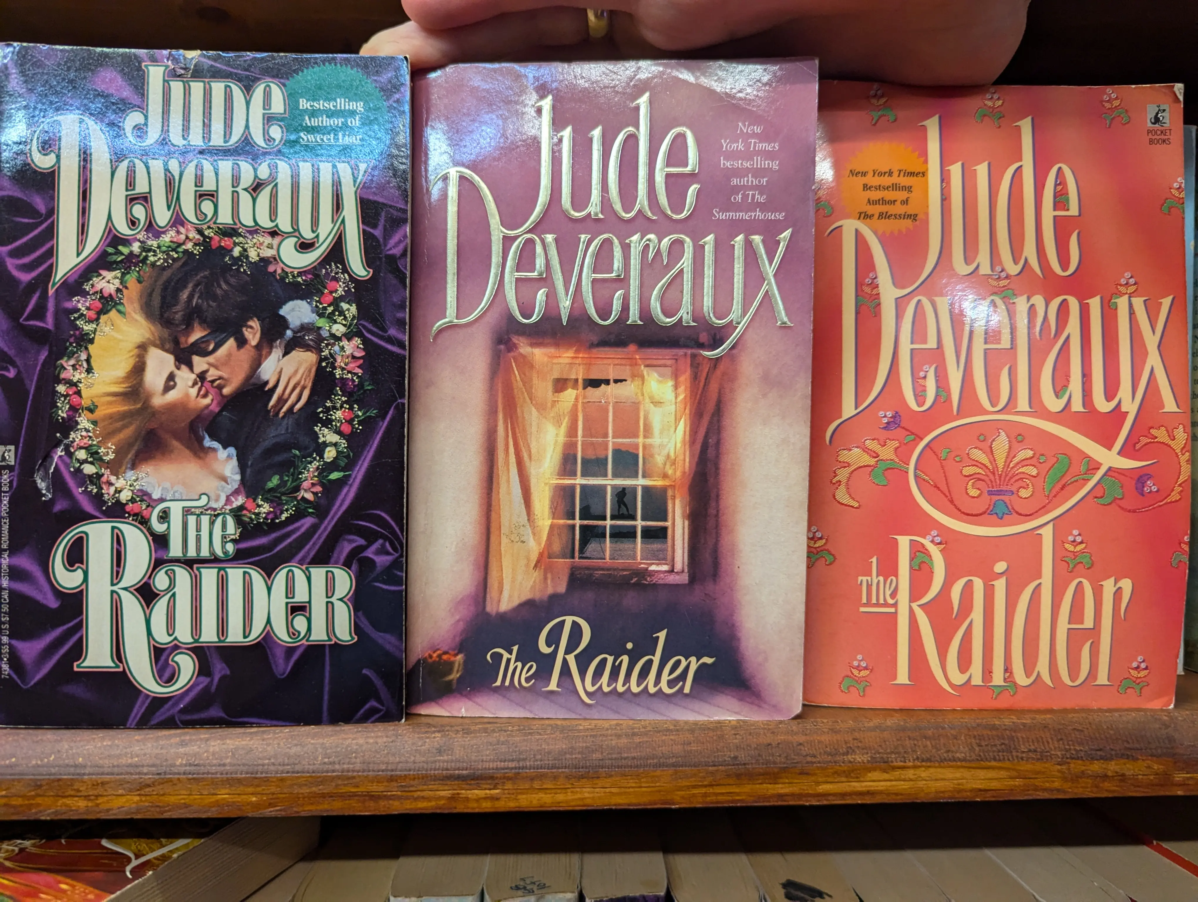 Jude Deveraux's The Raider, starting with a vignette of two people one with an eye mask on about to kiss, then a window with a gold curtain, and then some kind of flowers scattered on a coral background 