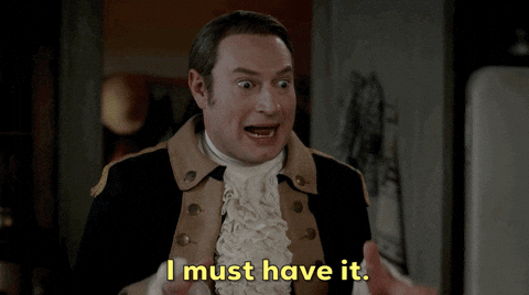 White dude in a lacy cravat and napoleonic jacket possibly from the show Ghosts holds both hands up in a grabby fashion and says I must have it.