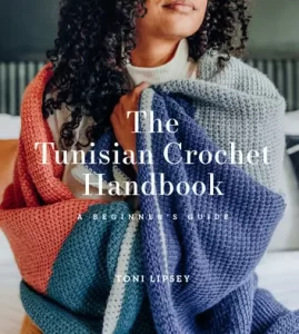 The Tunisian Crochet Handbook by Toni Lipsey - the cover is a picture of a woman with light brown skin and dark curly hair wrapped in a color block crochet blanket in blue, grey, coral, and teal