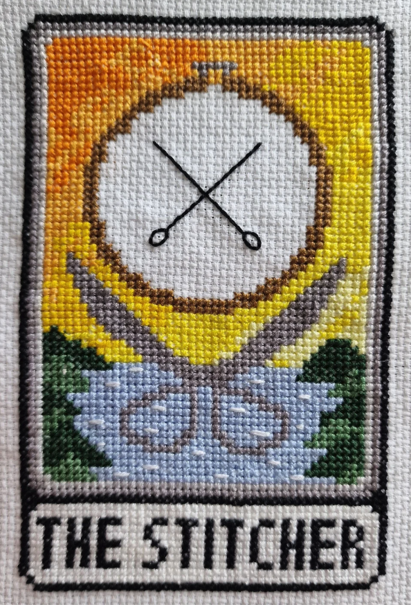 The Stitcher - a pair of scissors open beneath a sun with two crossed needles, with water and trees below