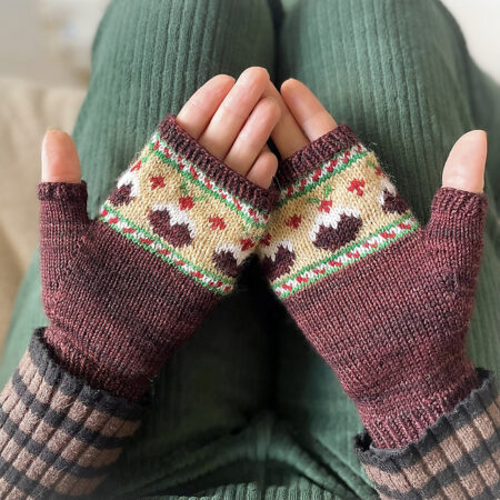 A pair of fingerless mitts that are mostly brown with green and red striping and Christmas pudding on a gold background