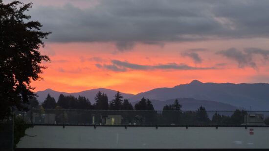 An orange and red sky beneath some clouds with a line of mountains beneath the orange and red