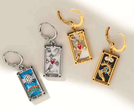 Four tarot card charms done in plated gold, enamel and with tiny stones attached to huggie hoop earrings. 