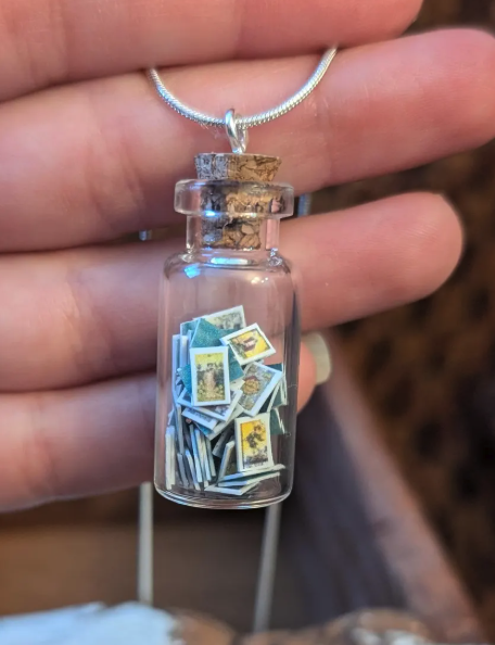 A hand holding a miniature jar pendant full of miniature tarot cards
