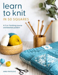 Learn to Knit in 50 Squares by Anna Pantelous a wood desk with knitting supplies and a blue and white block blanket folded across the desk