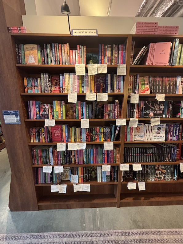 A bookcase full of books, spine out, with white shelf talker tags about three to five tags per shelf 