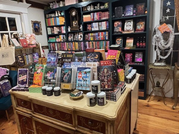 An interior shot of Montgomery and Taggert with black bookshelves and a table full of books and candles and other treats. it is full without looking cluttered