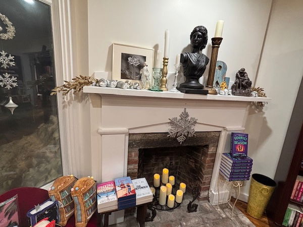 A fireplace with candles, and books in front and on the mantel
