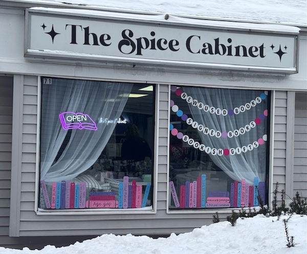 The Spice Cabinet front window with purple books painted on the glass. the sign is black on grey
