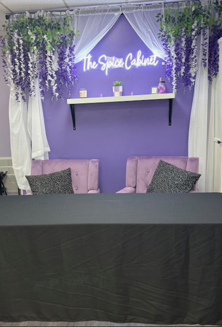 The Spice cabinet in neon against a purple wall with faux wisteria on either side