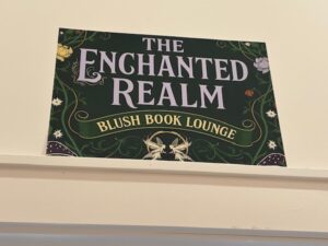 The Enchanted Realm sign with a green background and pink and yellow filigree and flowers around it