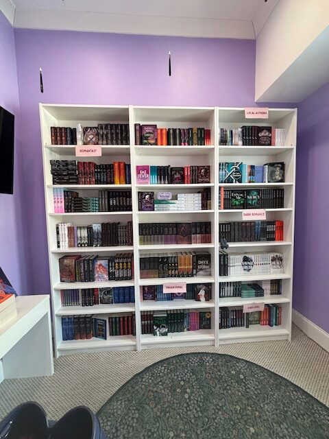 A purple wall with a white bookcase filled with books. There are candles suspended from the ceiling