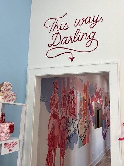 A sign pointed above a doorway reads in red script THIS WAY DARLING