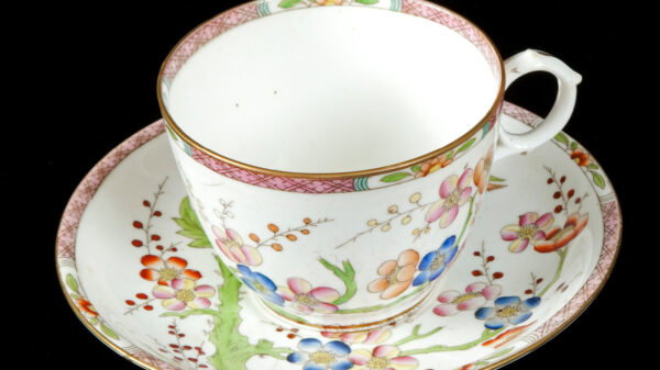 White teacup on a white saucer, both with a pattern of orange, pink, and blue flowers and a stripe around each rim