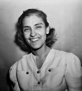 Black and white photo of Emma Tenayuca as a teenager. She has shoulder length wavy hair and is wearing a white dress with buttons and a V neck