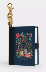 A dark blue leather and canvas edition of Sense and Sensibility by Jane AUsten with a pink and yellow floral illustration on the front, suspended by a brass hook clasp with a Coach tag