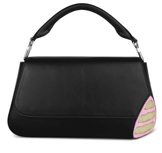 A black leather handbag with a trapezoidal shape and a short handle, with a corner cut out that looks like vanilla cake and strawberry icing