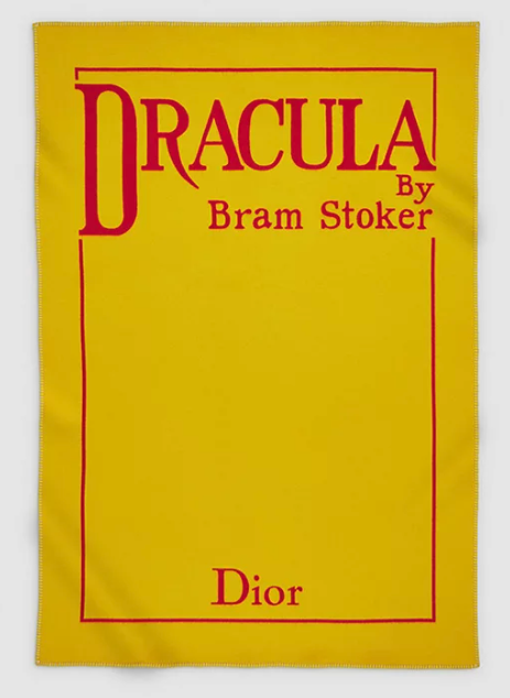 A rectangular yellow blanket with the words DRACULA by Bram Stoker at the top in red, with a red line frame and the word Dior at the bottom.