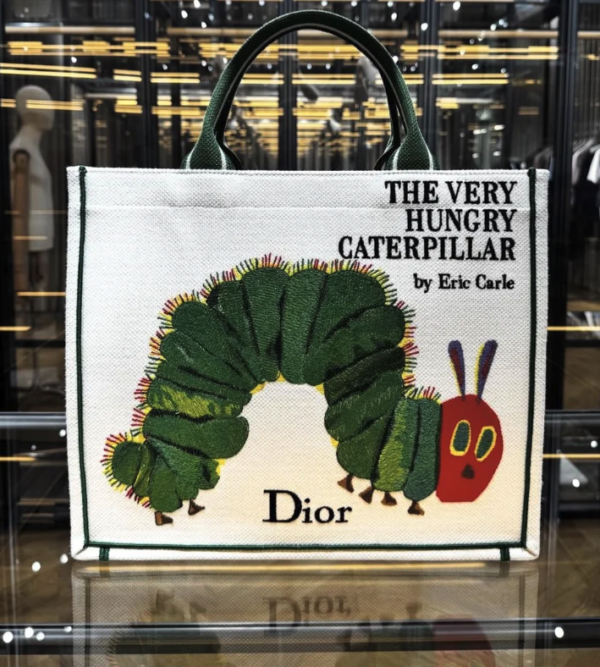 A white woven book tote with leather handles and the cover of Eric Carle's The Very Hungry Caterpillar on the side 