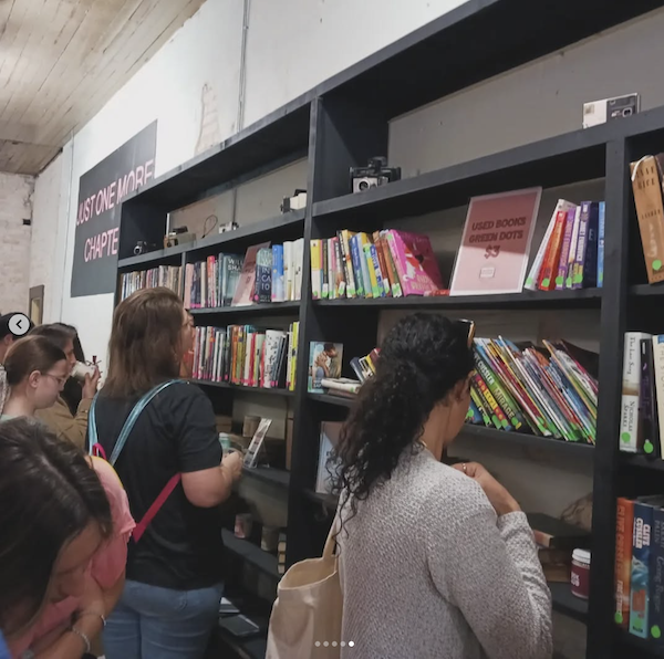 People standing in front of a used books shelf examining the books. the shelves are black against a white wall 