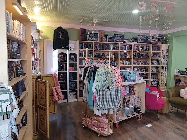 A section of the bookstore showing shelves of books plus merch in the form of sweatshirts, tees, and totebags.