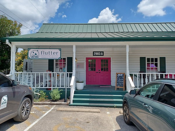 Flutter Bookshop, a white building with a porch, green roof and steps, and a bright pink door 
