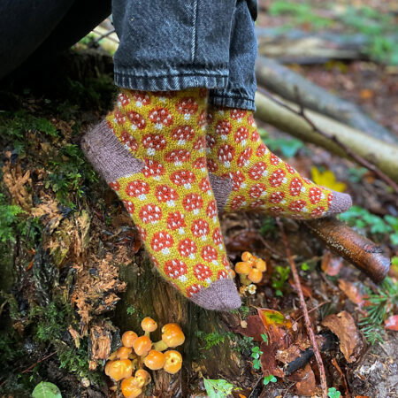 Colorwork socks with red and white mushrooms against a green background