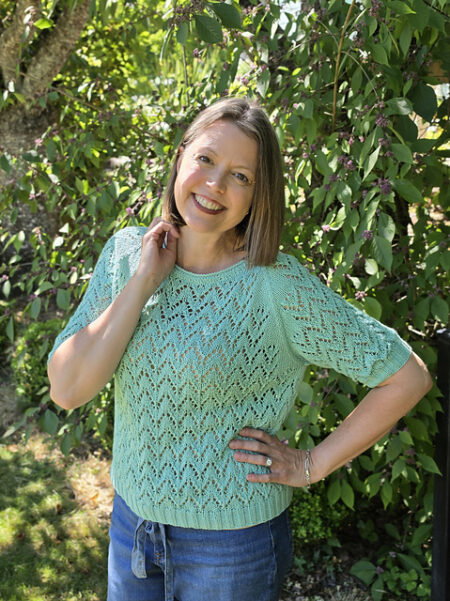 A woman wears a lacy half sleeved sweater in a pale blue-green.