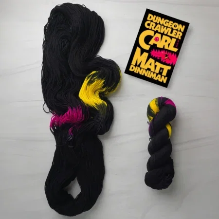 Black yarn with neon pink and gold pooling and a copy of Dungeon Crawler Carll
