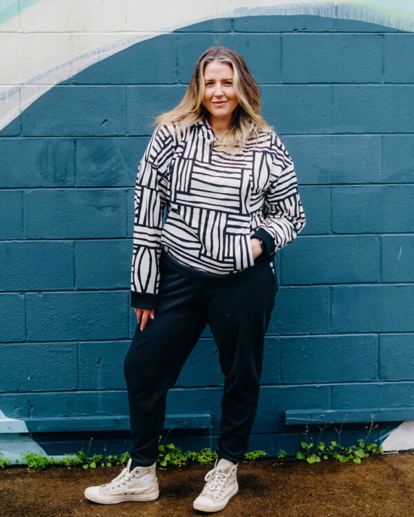 A white woman with blonde and brown hair wears a tracksuit with a pocked hoodie top in a blue and white print, and blue joggers