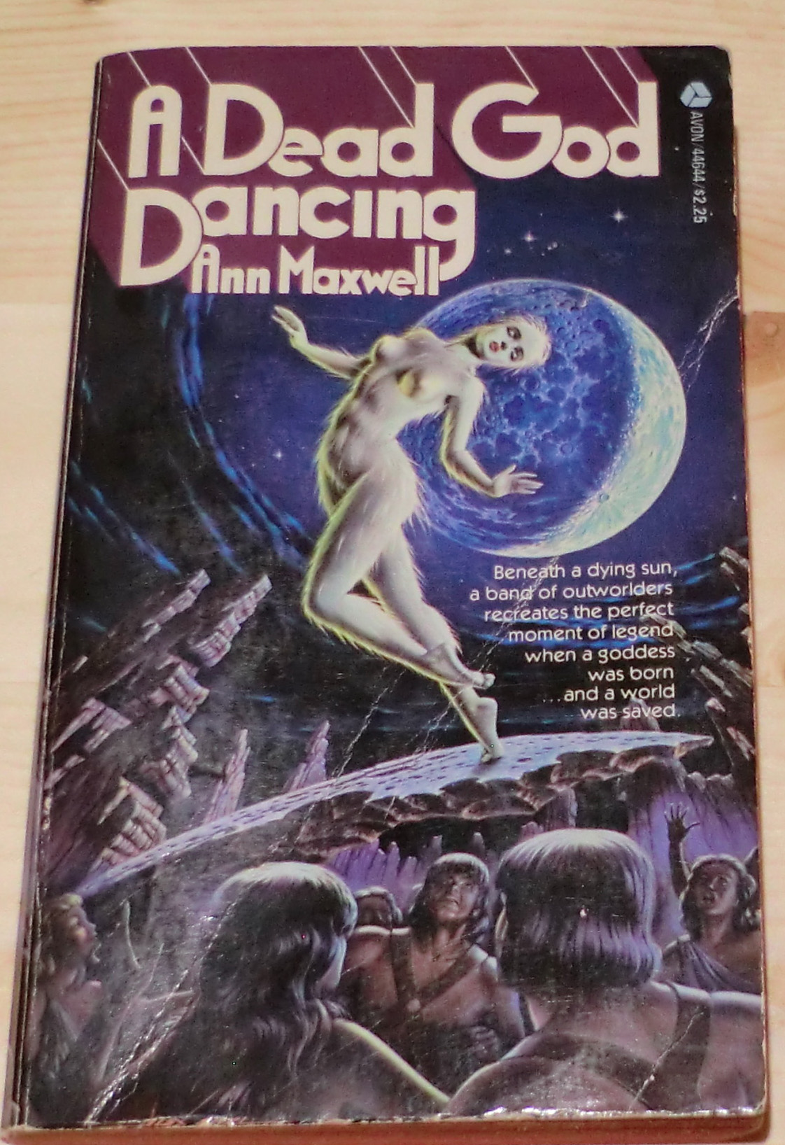 A dead god dancing - a pale white woman who looks like she's naked and covered with feathers dancing above a group of long haired angry primitive-looking men