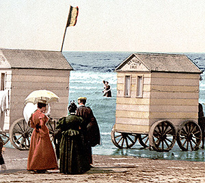 Women outside a bathing box a small shed on wheels with high frosted windows that is rolled into the surf
